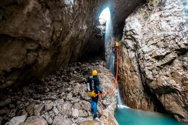 A group of canyoneers climbing down a waterfall in a lagoon-like cave formation.