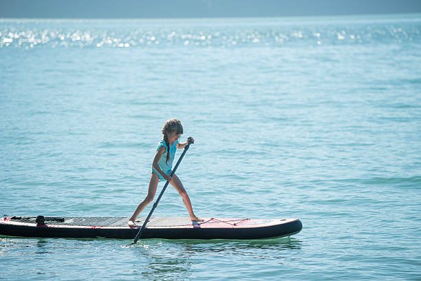 Young girl paddles SUP board on lake in summer