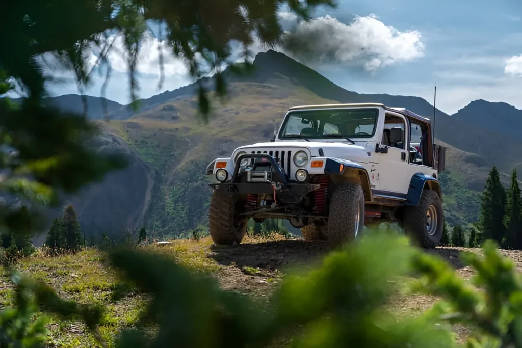 An off-road vehicle rests on a mountain trail, showcasing rugged terrain and natural beauty. The setting exemplifies outdoor adventure and exploration, with greenery and imposing mountains forming the backdrop.