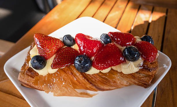Croissant with cream, blueberries and strawberries lies on a plate, on a table, in a summer cafe in armenia